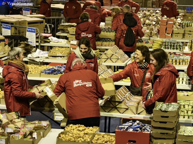 Vue d'ensemble de la préparation des sacs : une dizaine de bénévoles se passent les cartons le long des tables.