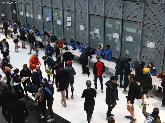 Le hall au plus fort du retrait des dossards, coureurs devant la longue table des bénévoles.