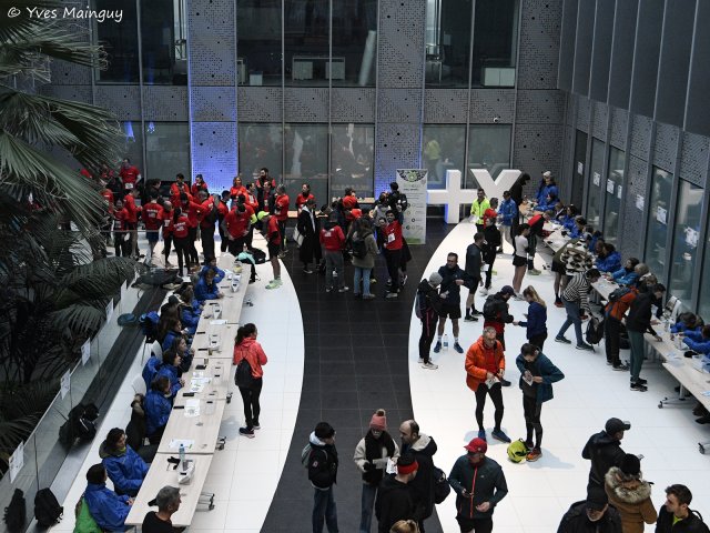 Vue plongeante sur la courbe des tables de retrait et le groupe des bénévoles rassemblés au fond.