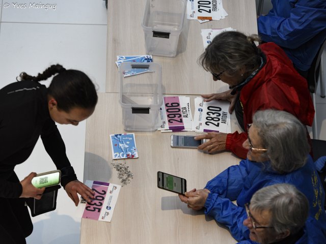 Deux bénévoles cherchent un dossard dans un bac, un téléphone à la main pour vérifier le numéro.