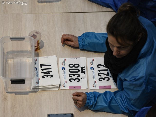 Un bénévole trie des dossards nominatifs dans un bac de rangement.