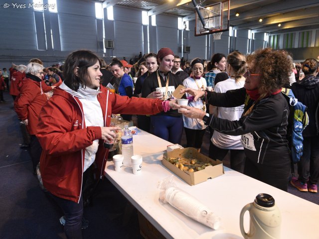 Au ravitaillement d'arrivée, une bénévole tend un gobelet par-dessus la table.