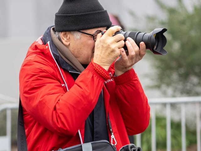 Un photographe de la course, bonnet et veste rouge, l'œil au viseur.